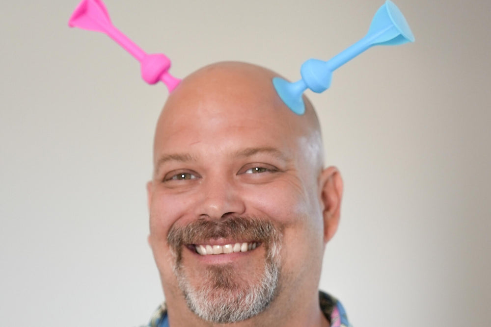 A smiling Tossit team member with two suction-cup darts stuck to his head