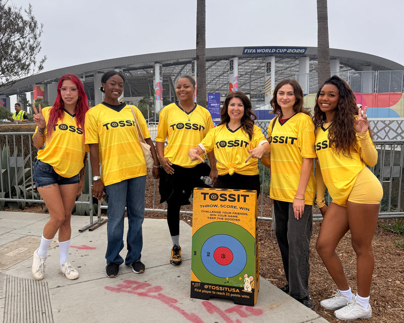 Six people in TOSSIT shirts beside a branded target stand outside the stadium at the FIFA World Cup 2026